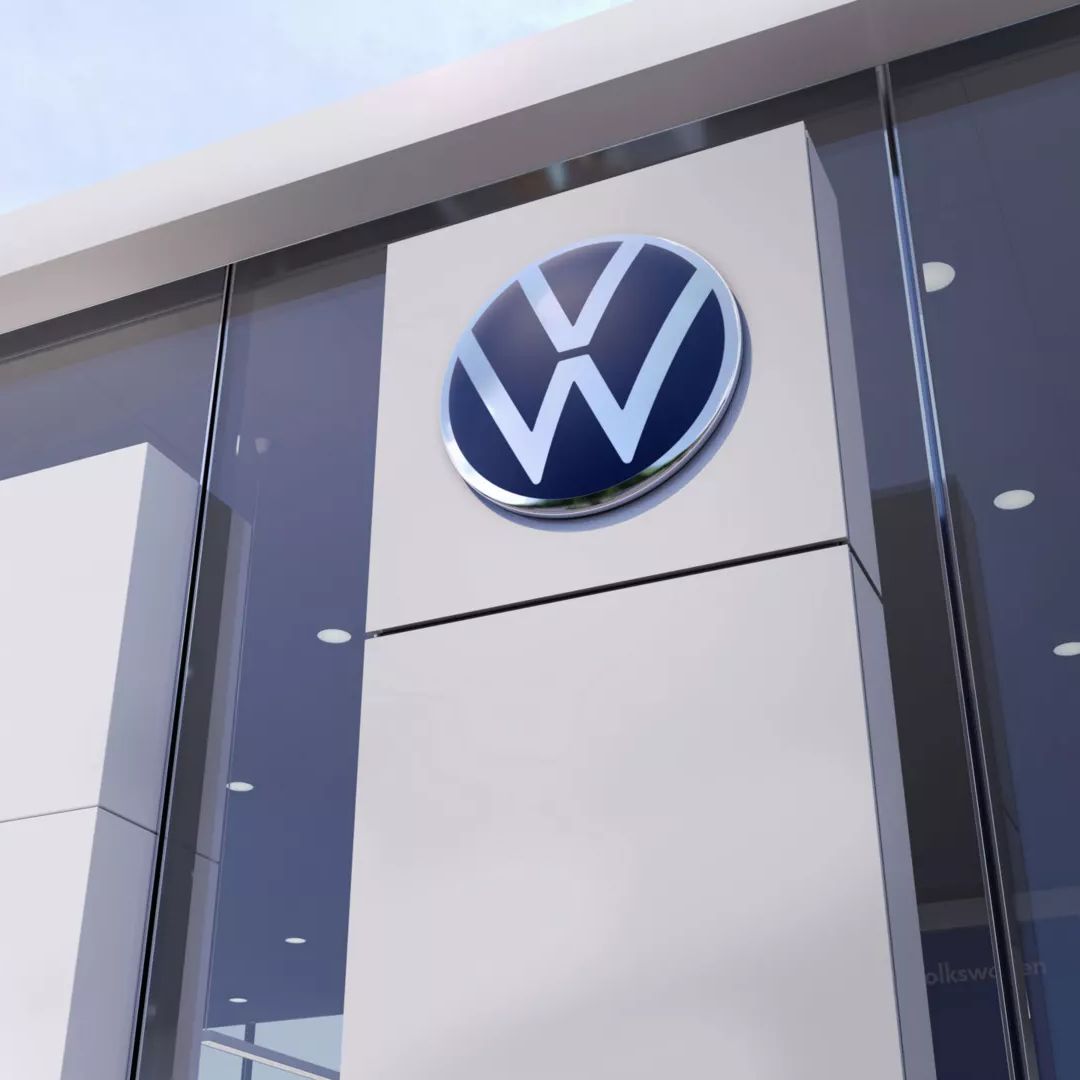 Stekleno pročelje sodobne stavbe z velikim logotipom Volkswagna, ki visi nad vhodom.