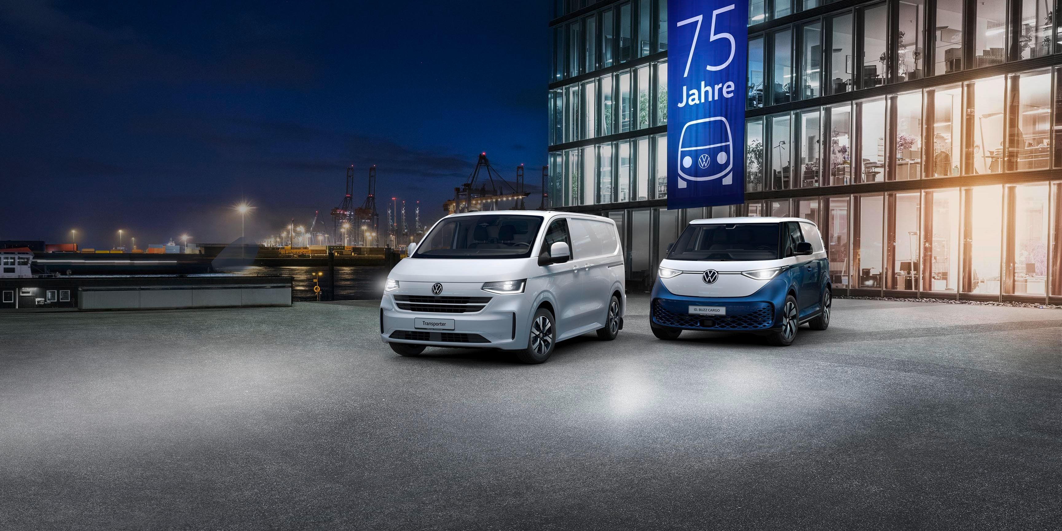 Parkirani sta dve Volkswagnovi dostavni vozili pred sodobno stekleno stavbo. Na stavbi je velika modra reklamna tabla z napisom "75 Jahre". V ozadju so vidni gradbeni žerjavi in pristanišče.