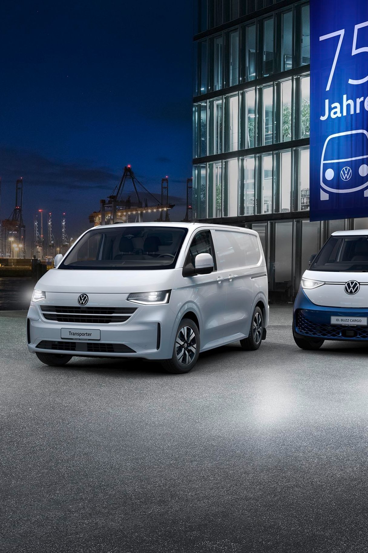 Parkirani sta dve Volkswagnovi dostavni vozili pred sodobno stekleno stavbo. Na stavbi je velika modra reklamna tabla z napisom "75 Jahre". V ozadju so vidni gradbeni žerjavi in pristanišče.