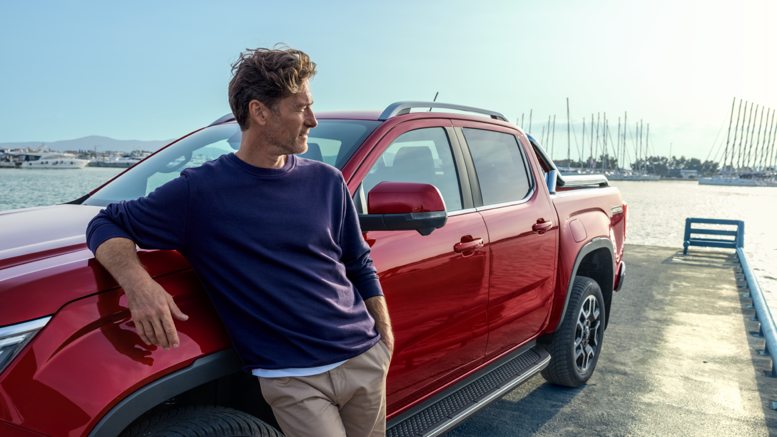 Mann lehnt an neuem Amarok, der am Hafen steht, und blickt über das Wasser