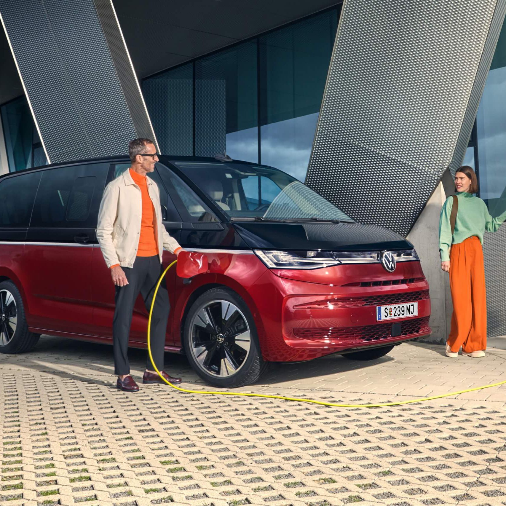 Zwei Leute laden ihren elektrischen New Multivan, der rot- schwarz ist 