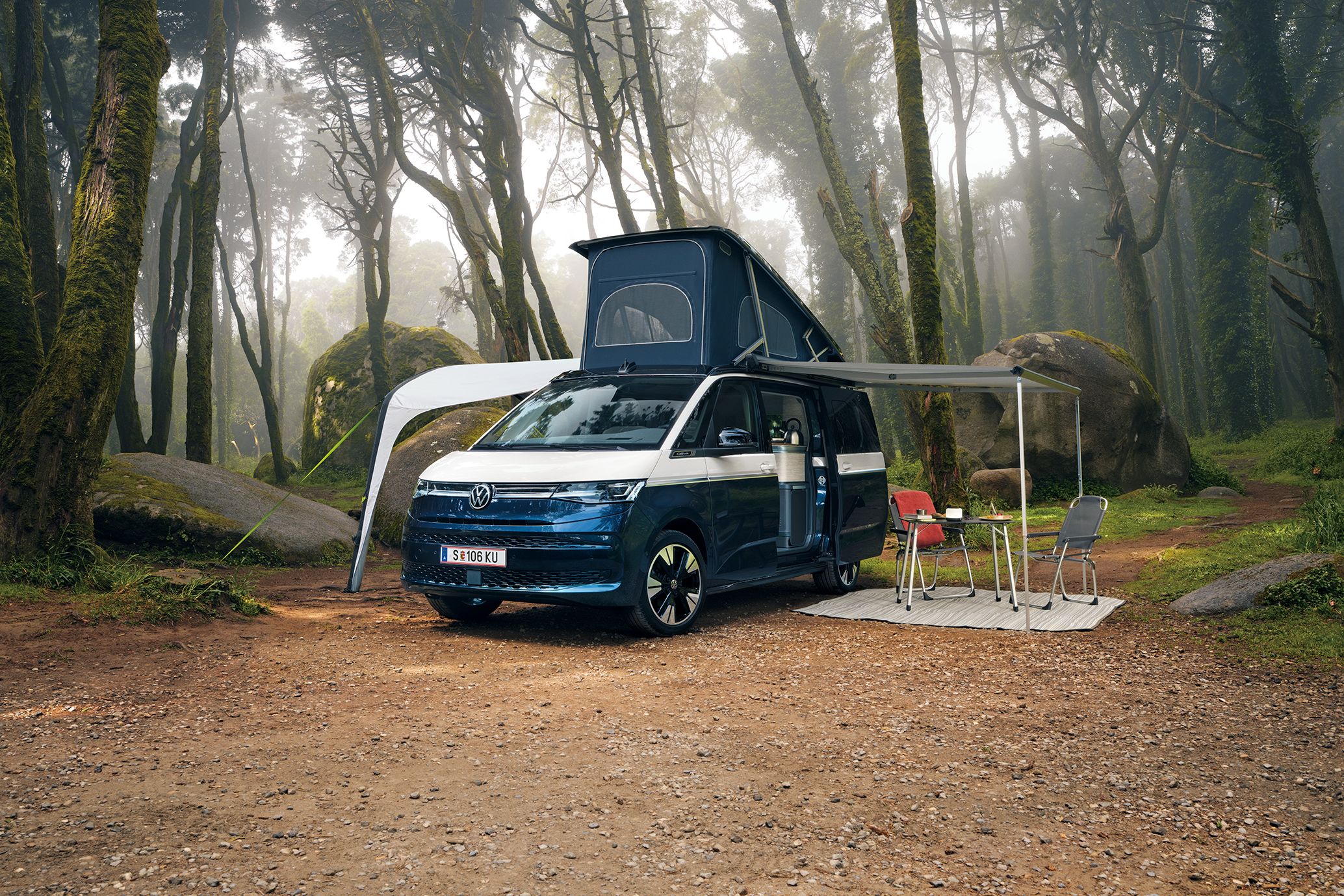 New California steht mit ausgeklapptem Dach und ausgefahrener Marquise in einem Wald, Campingstühle stehen unter der Marquise