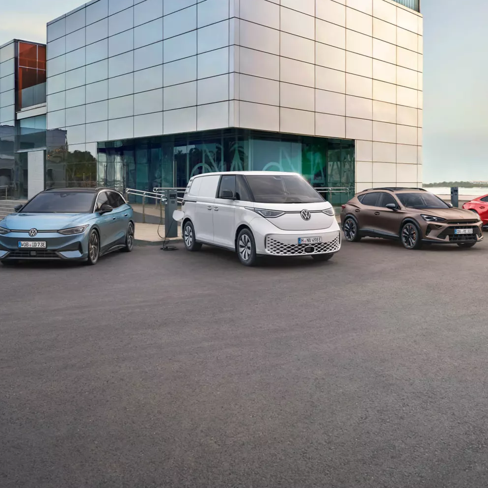 Eine Reihe von Fahrzeugen steht vor einem modernen Gebäude. Es sind verschiedene Autotypen, darunter Limousinen, ein Van und ein Sportwagen. Die Autos sind in unterschiedlichen Farben lackiert.