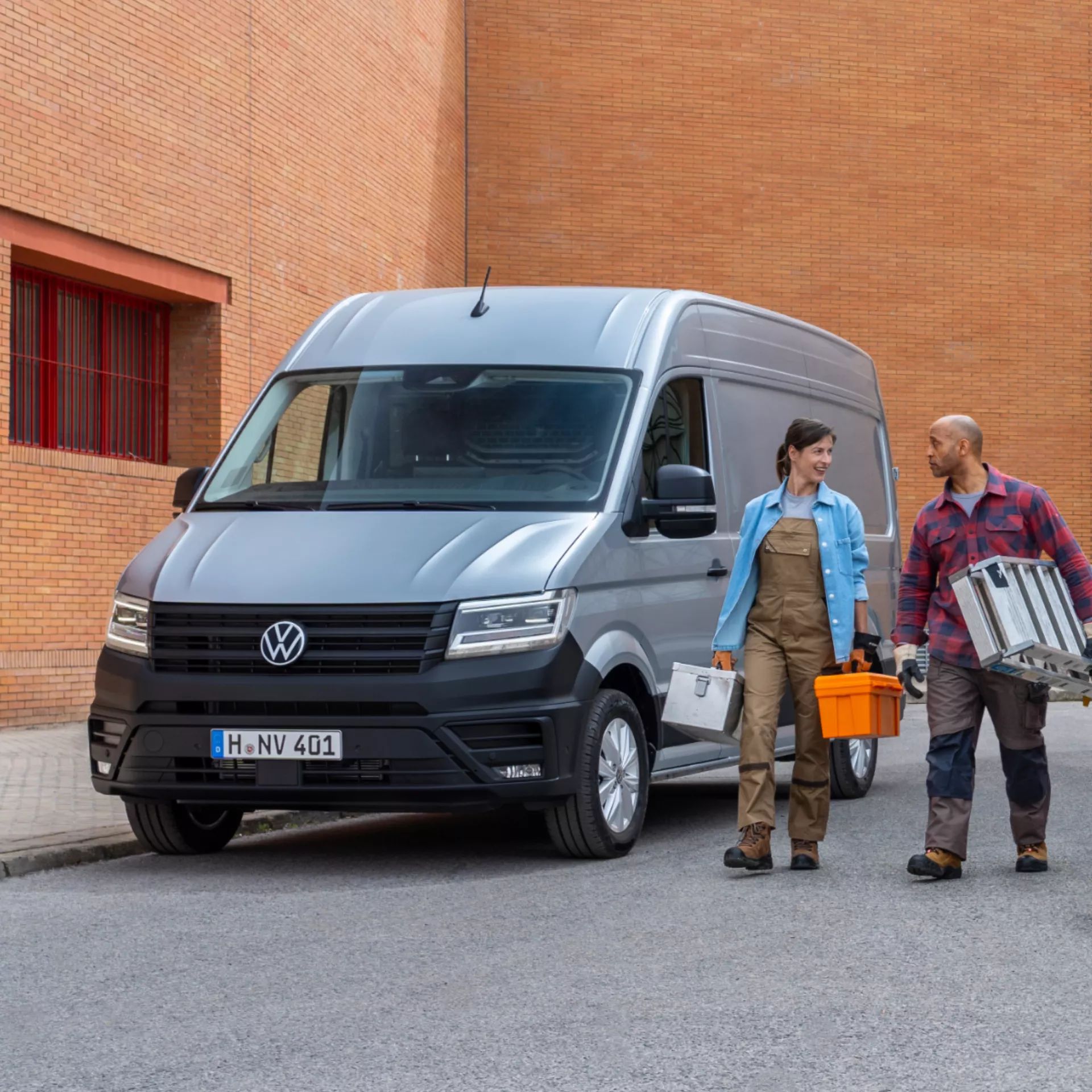 Zwei Handwerker gehen an einem silbernen VW Crafter vorbei