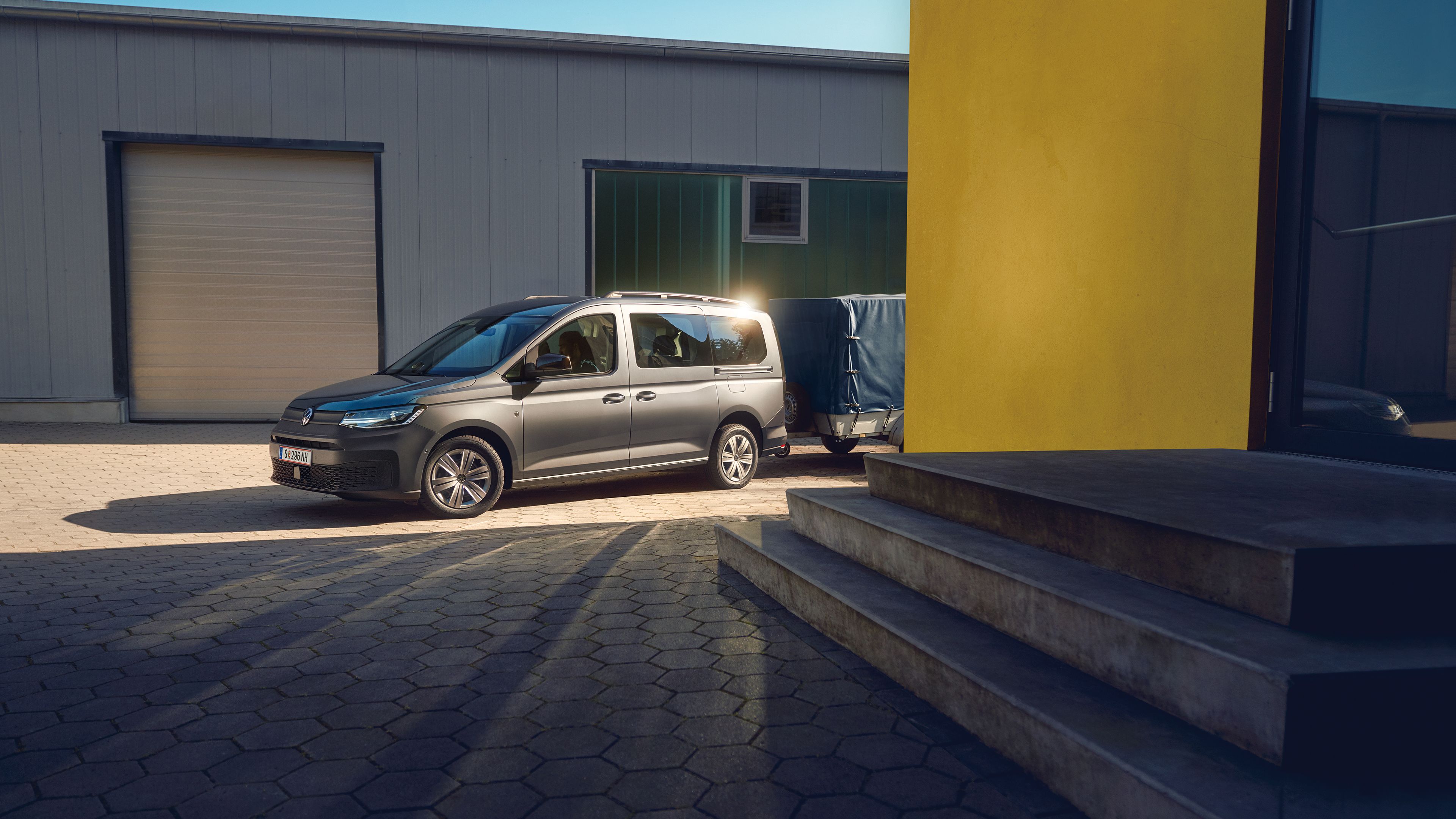 Ein grauer VW Caddy mit Anhänger parkt neben einer Garage