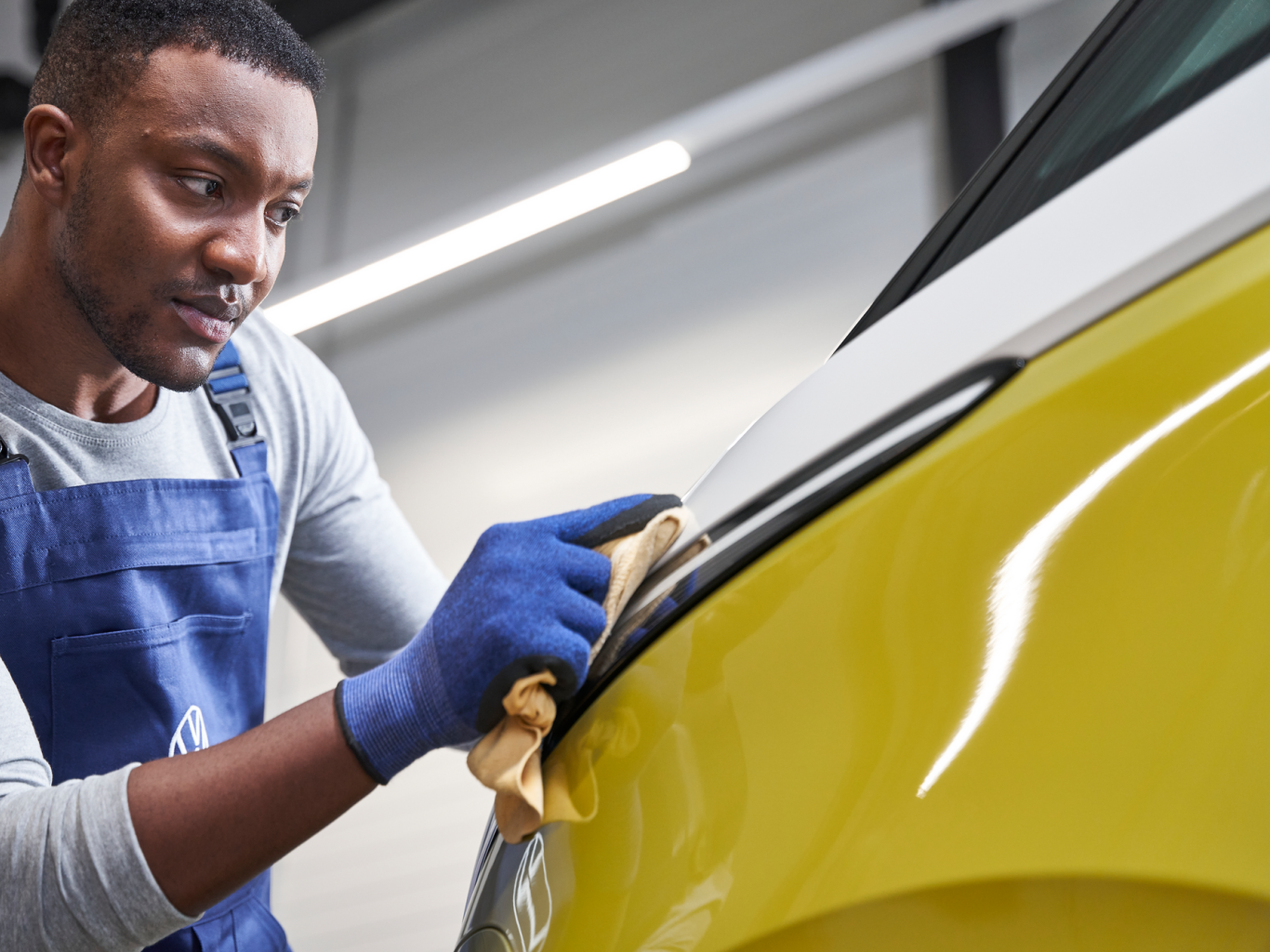 Moški v delovni obleki polira rumen VW ID.Buzz.