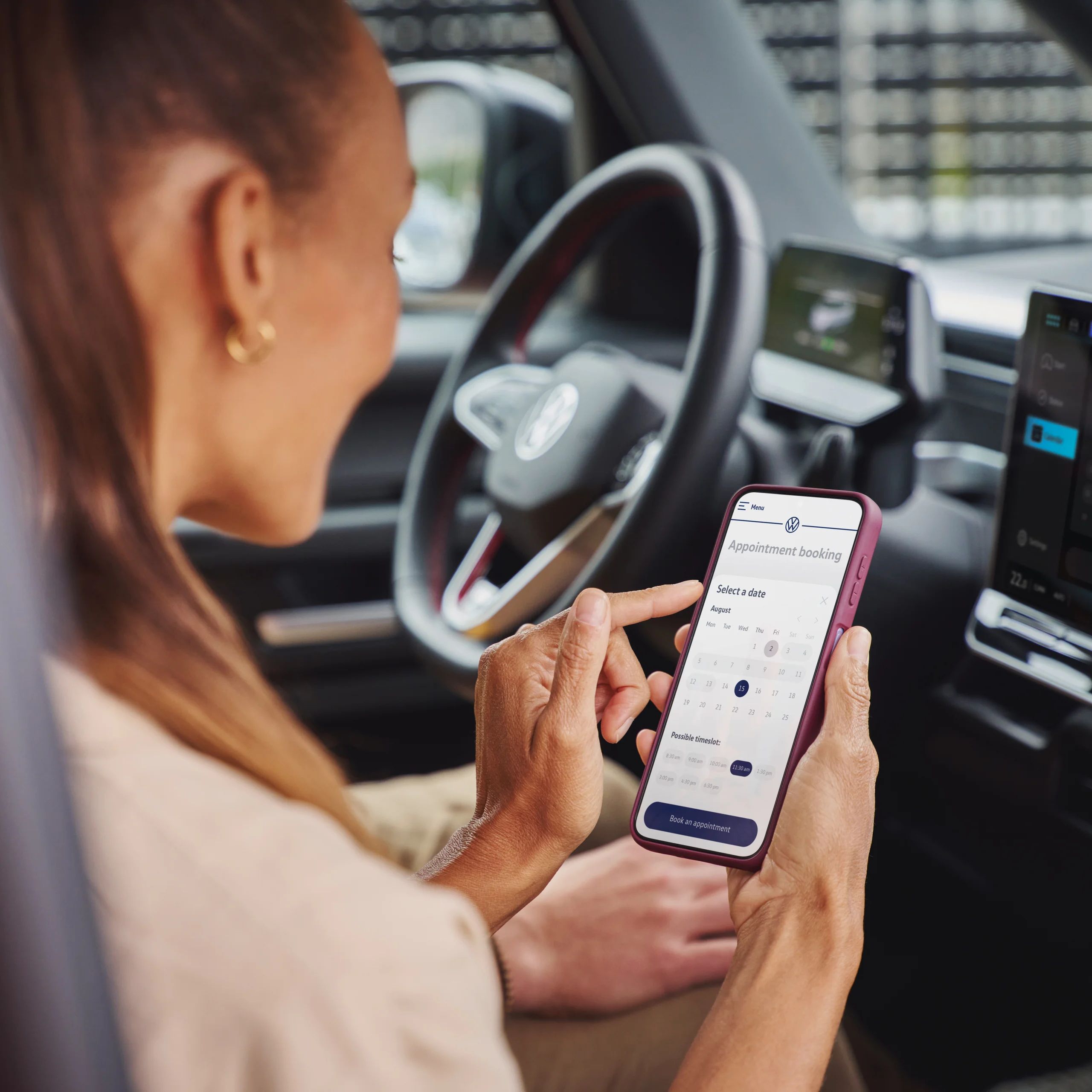 Oseba v avtomobilu uporablja pametni telefon za upravljanje aplikacije na dotik. V ozadju je volan in zaslon avtomobila z različnimi prikazi.