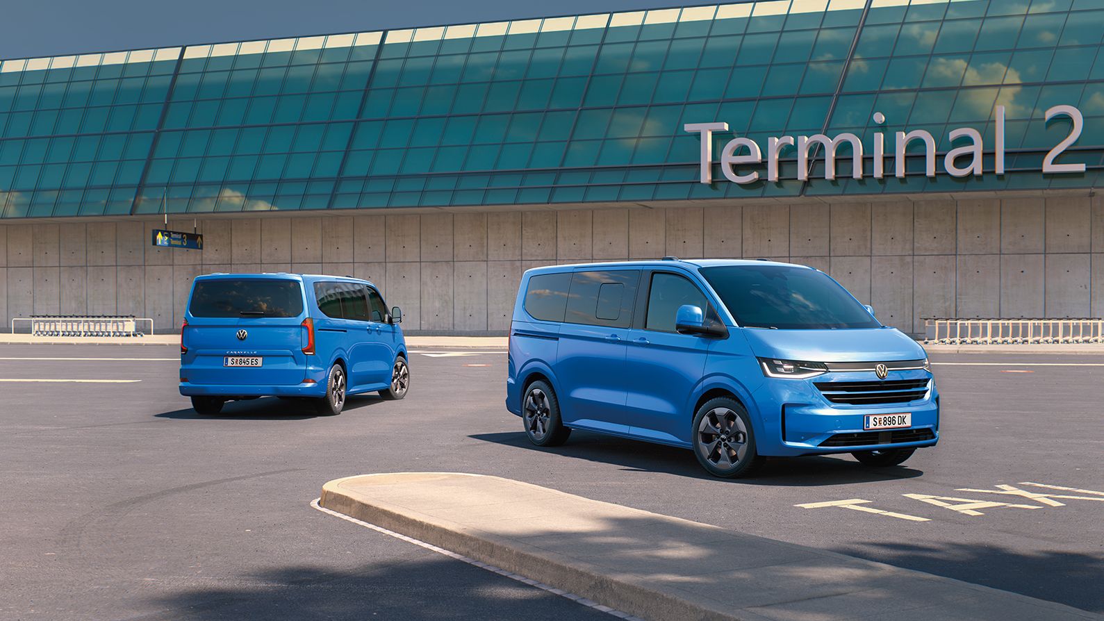 Zwei VW Caravelle stehen vor dem Terminal 2 auf einem Flughafenparkplatz