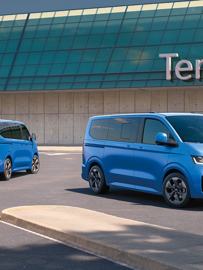 Zwei VW Caravelle stehen vor dem Terminal 2 auf einem Flughafenparkplatz