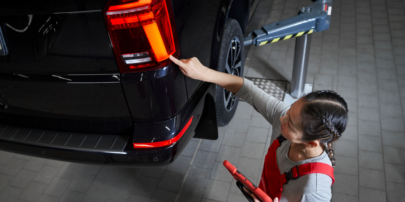 Eine VW Service Partnerin begutachtet die Heckleuchten eines VW Nutzfahrzeugs