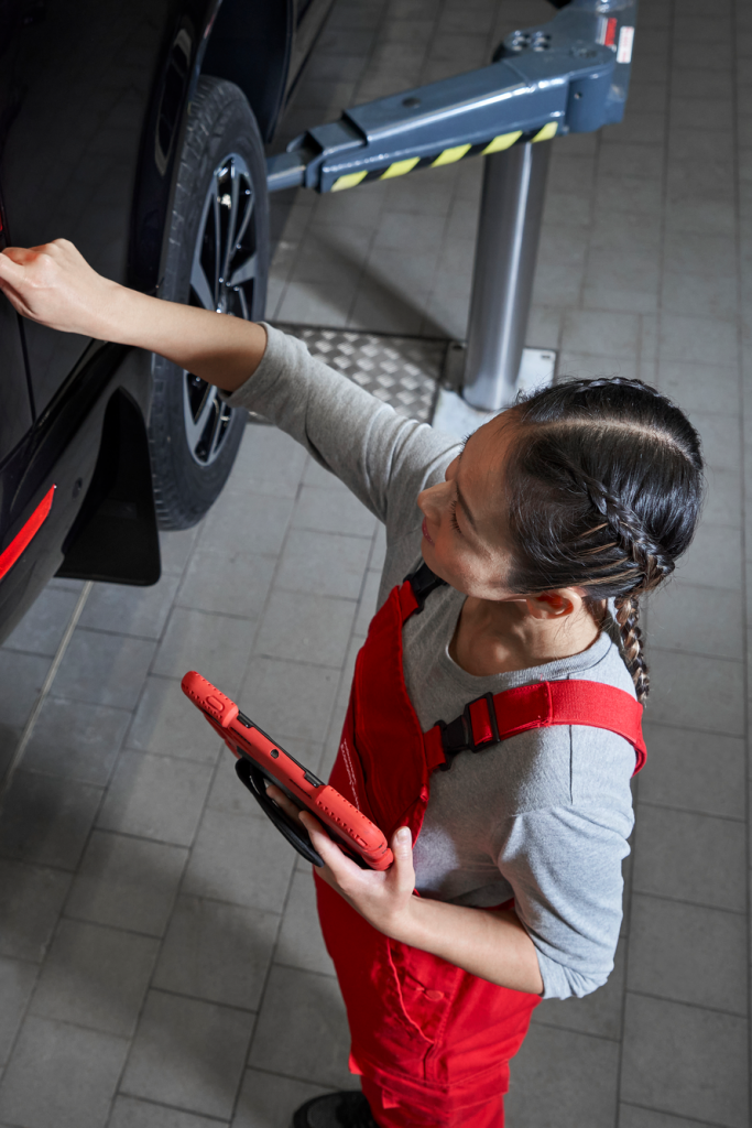 Eine VW Service Partnerin begutachtet die Heckleuchten eines VW Nutzfahrzeugs