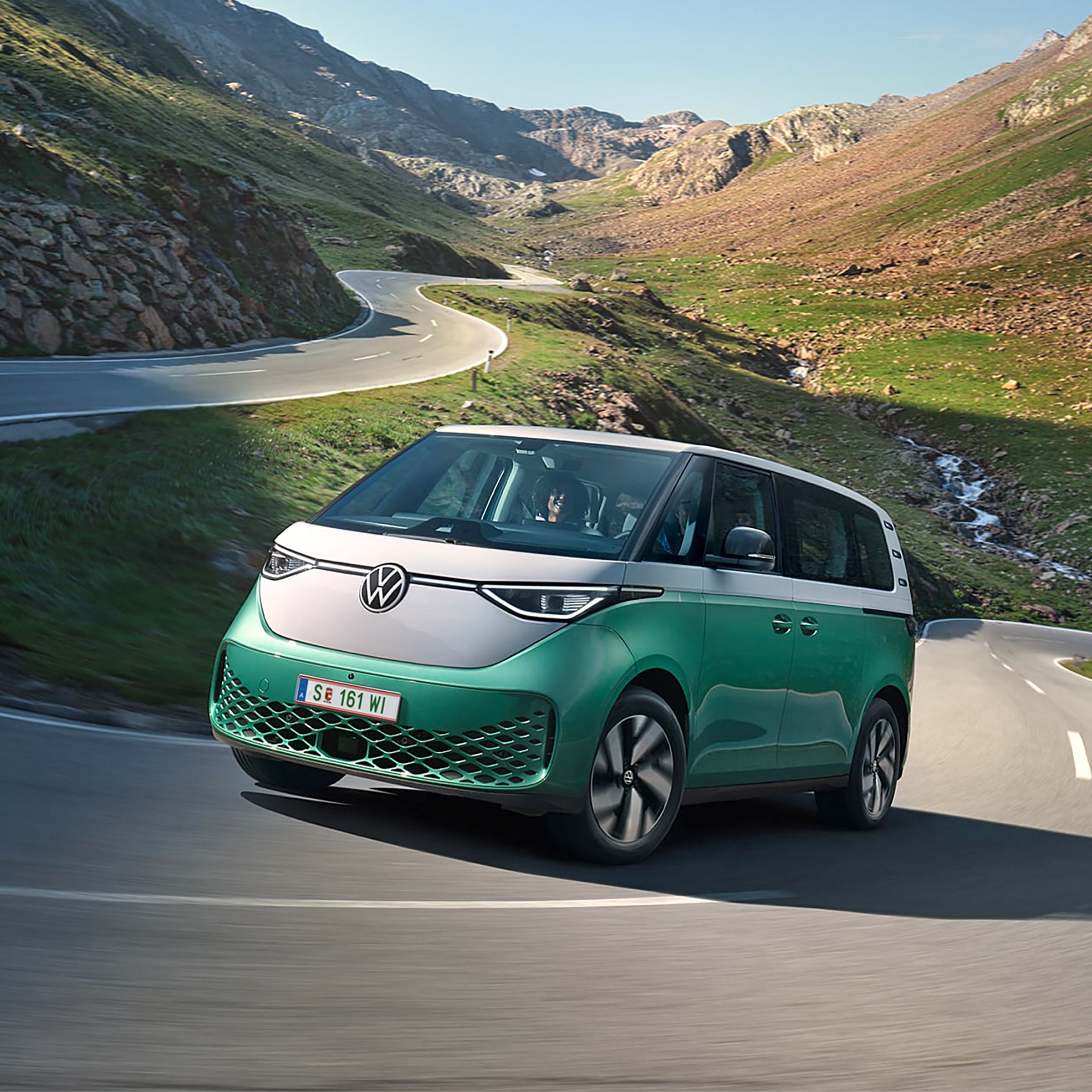 Ein grün weißer VW ID. Buzz fährt dynamisch in die Kurve einer kurvenreichen Bergstraße
