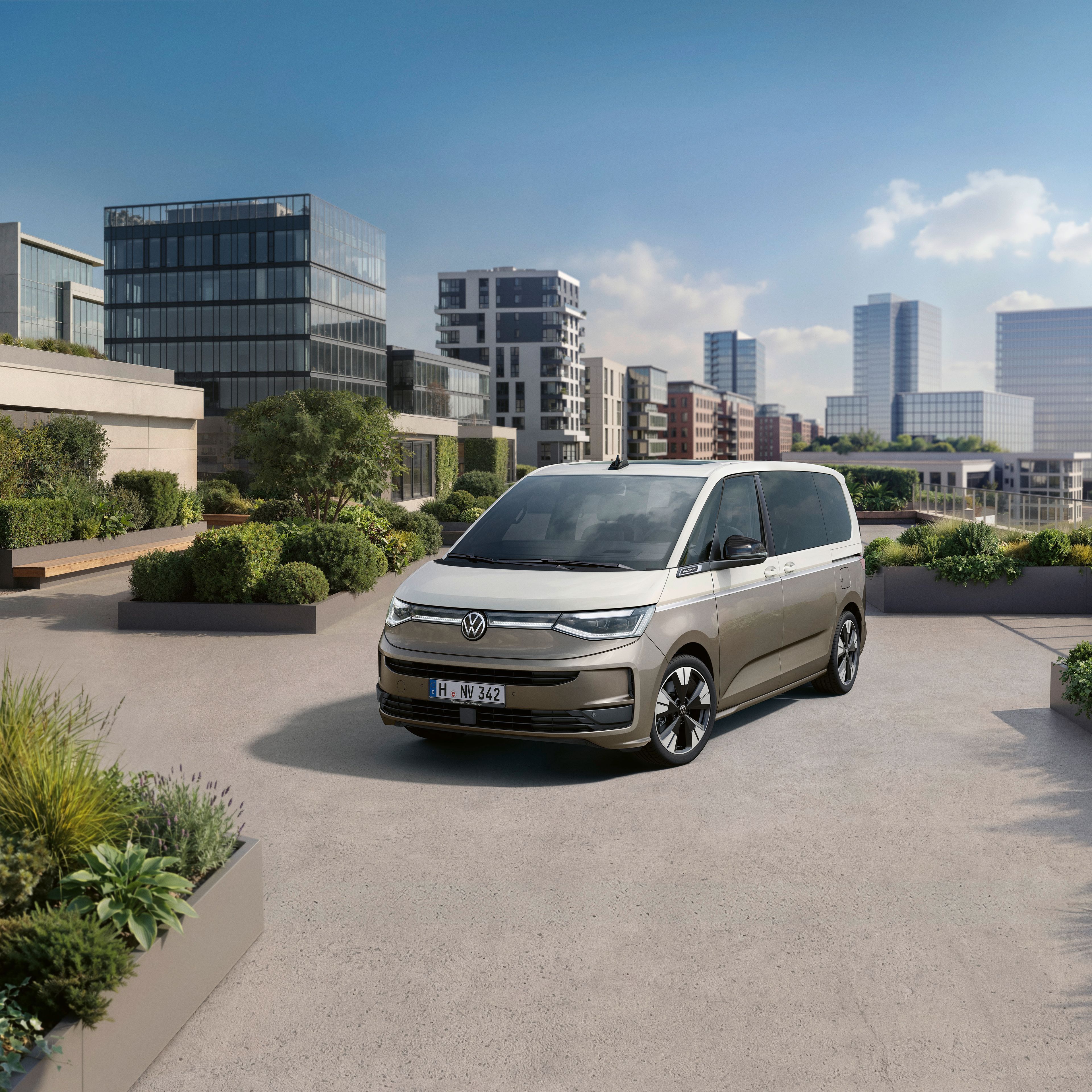 Sodobna srebrno-bež enoprostorec Volkswagen Multivan stoji na prostorni terasi z urejenimi zelenimi gredami. V ozadju so moderna poslovna in stanovanjska poslopja ter nebotičniki ob vodi pod jasnim modrim nebom. Atmosfera je urbana, mirna in sončna.