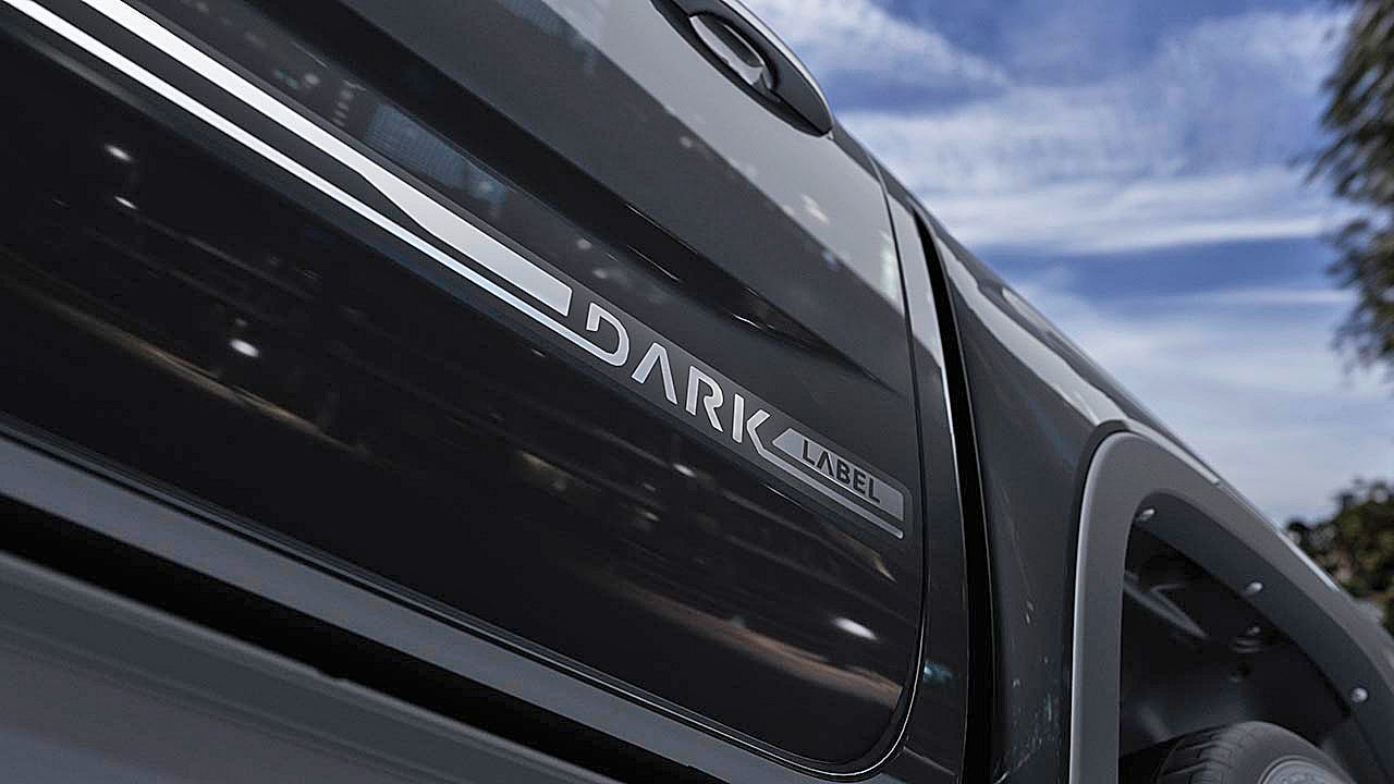 Nahaufnahme eines schwarzen Autos, auf dem der Schriftzug "DARK LABEL" zu sehen ist. Die Aufnahme betont die glänzende Oberfläche des Fahrzeugs. Im Hintergrund ist ein blauer Himmel mit einigen Wolken zu erkennen.