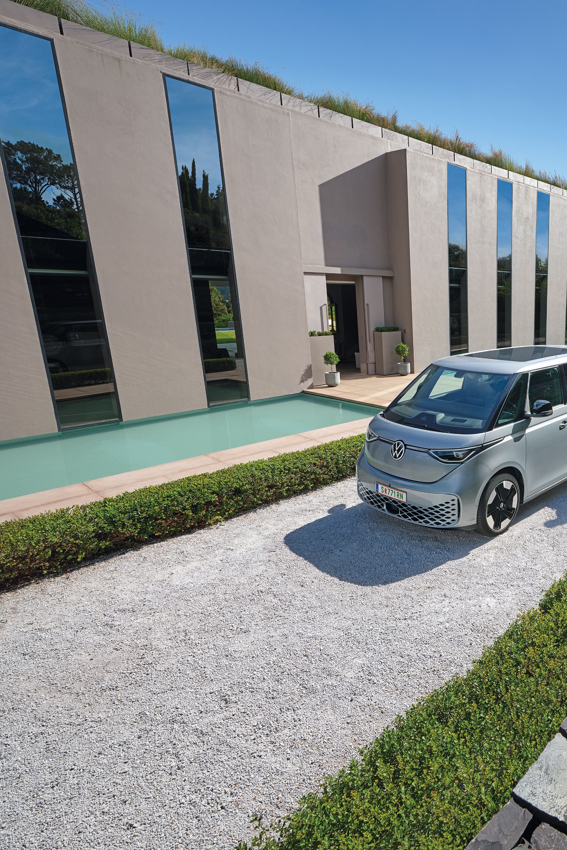 Ein silberner ID. Buzz parkt vor einem modernen Haus, ein Paar  geht auf das Auto zu