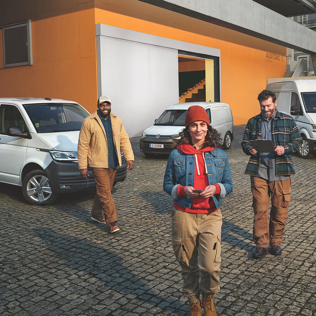 Weißer Crafter Kastenwagen, weißer Caddy Cargo und weißer Transporter Kastenwagen stehen auf einem Parkplatz vor einem Gebäude.