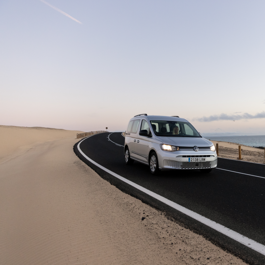 VW Caddy srebrne barve na cesti ob obali